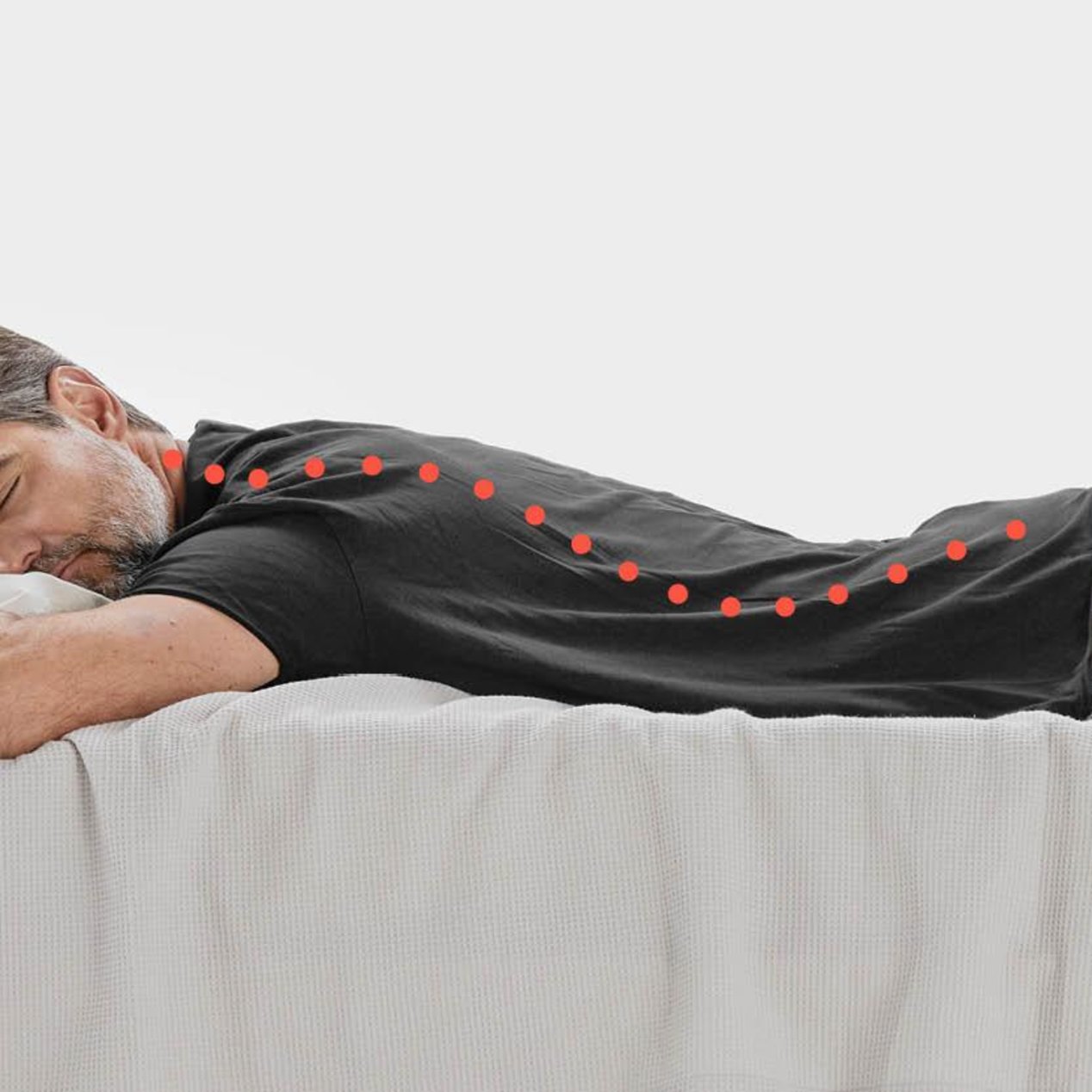 A man is lying face down in bed with his back curved