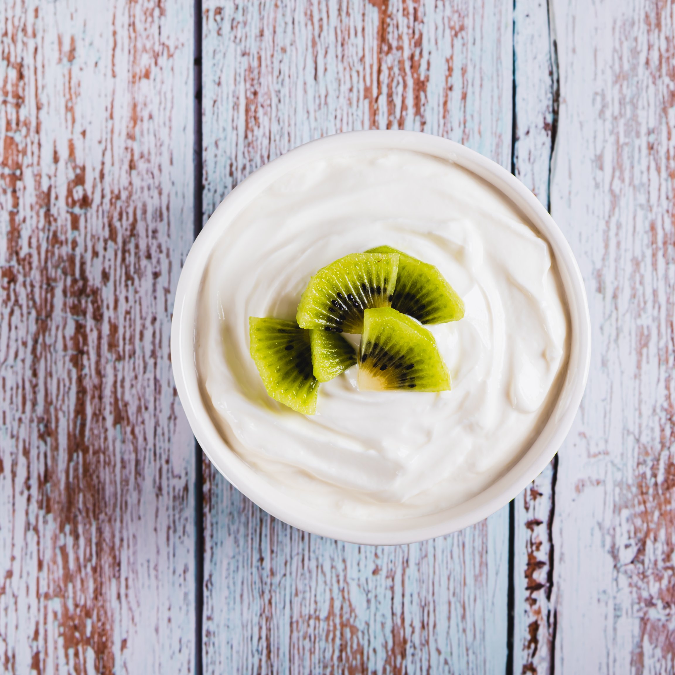 Nahaufnahme eines dickflüssigen, fermentierten Magermilchprodukts mit Probiotika und Kiwi in einer Schüssel, von oben auf einem Tisch fotografiert.