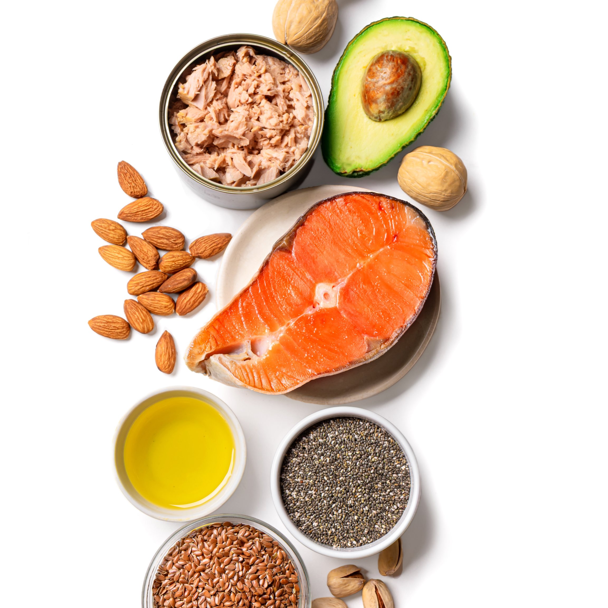 Draufsicht auf omega-3-reiche Lebensmittel wie Lachs, Thunfisch, Avocado, Mandeln, Walnüsse, Olivenöl, Chiasamen und Leinsamen auf weißem Hintergrund.