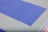 Nahaufnahme einer blauen Kunststoff-Gitterstruktur, eingebettet in eine hellgrüne Schaumstoffmatte. Sichtbare rosa und blaue Schichten an den Rändern erzeugen eine saubere, technische Optik.