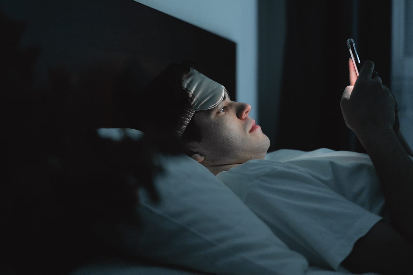 Mann schaut aufs Händy im Bett