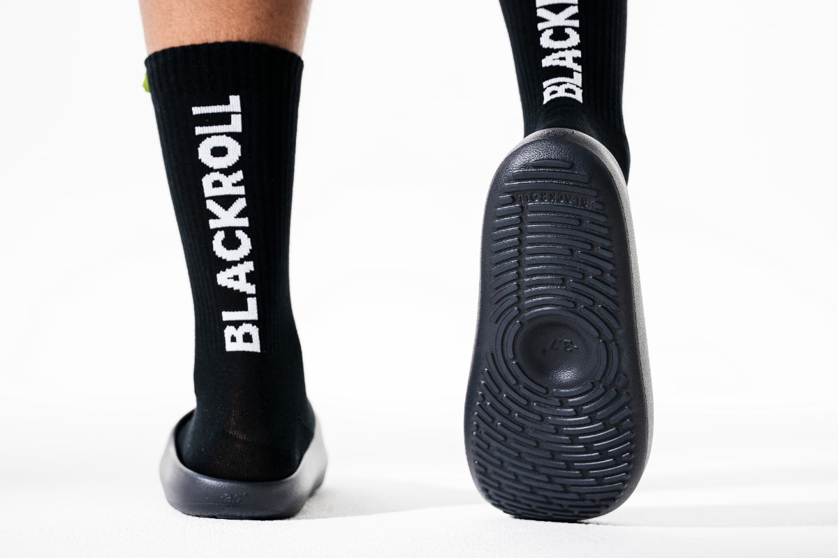 Person trägt schwarze BLACKROLL Socken und zeigt die profilierte Sohle der RECOVERY SLOPES CORE.