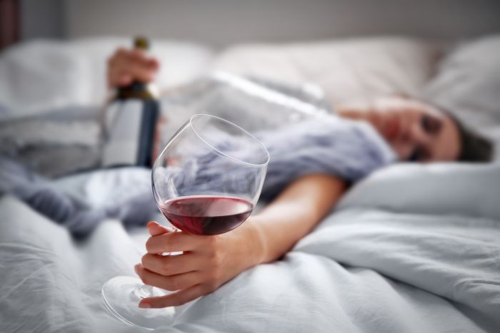 Schlafende Frau im Bett mit Rotweinflasche und -glas in der Hand