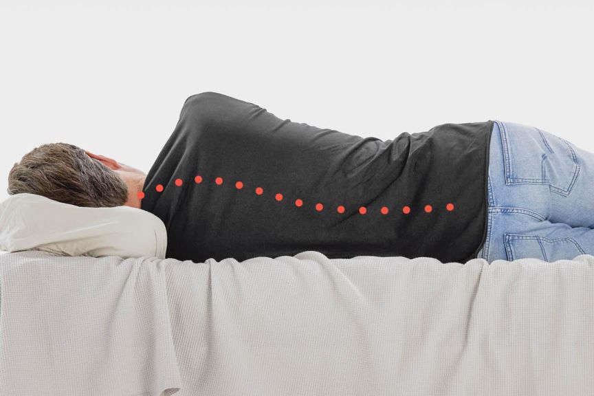 Ein Mann liegt im Bett in Seitenlage mit krummer Wirbelsäule