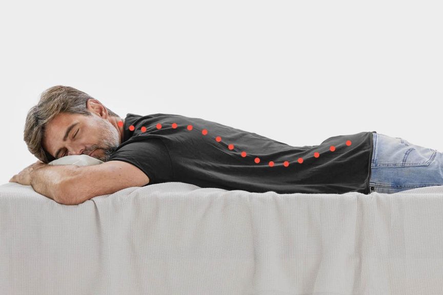 Ein Mann liegt im Bett in Bauchlage mit gebogenem Rücken